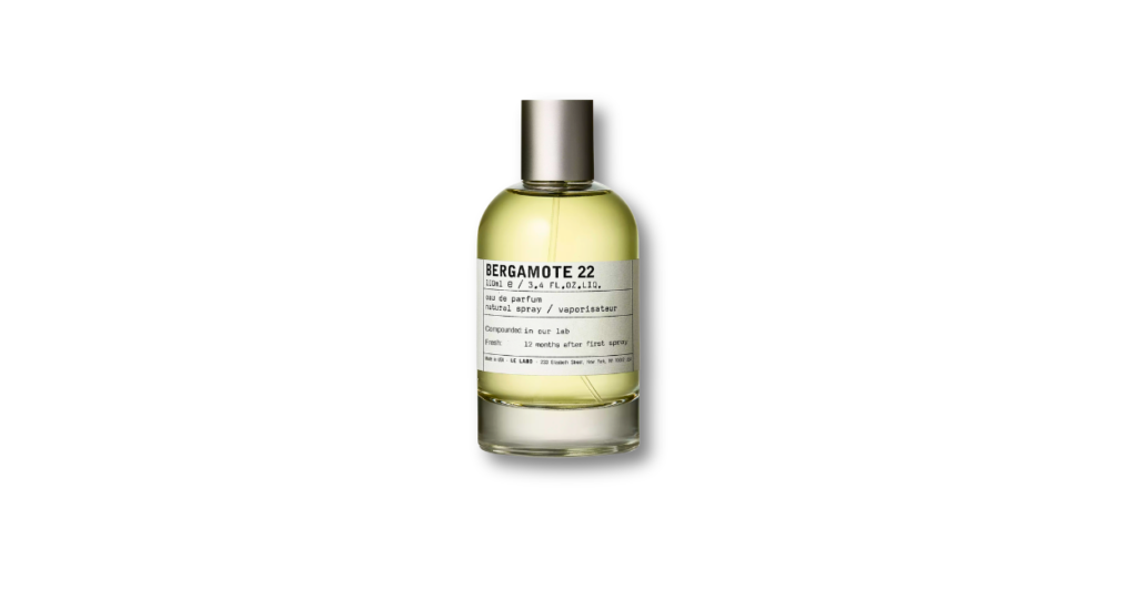 Le Labo Bergamote 22 fragrance bottle against a minimalist background, with fresh citrus slices and a sprig of green leaves, evoking a bright, unisex scent.