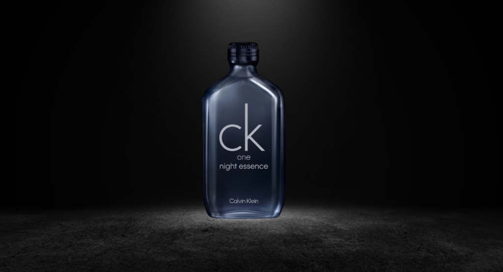 Close-up of CK One Night Essence bottle showing silver cap, black cylindrical glass, and minimal branding on dark background
